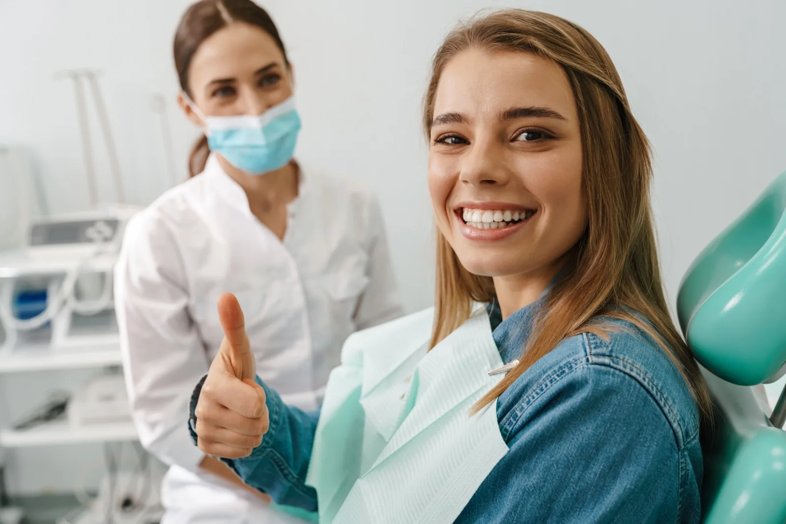 A relaxed dental patient giving a thumbs up beside her hygienist